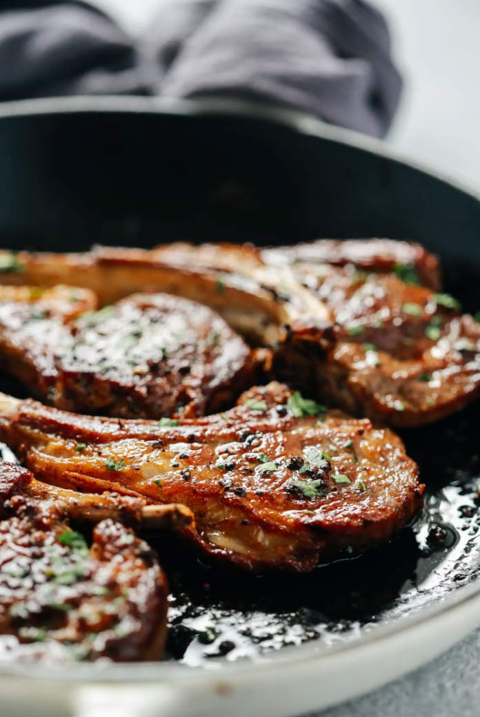 three lamb chops on a cast pan with herbs and butter for easy easter dinner